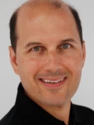 Headshot portrait of Dr. Simpson smiling in a black shirt against a light grey background